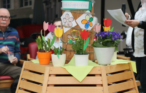 Pflanzendekoration mit bunten Blumentöpfen und Papierblumen in einem Erlebnisgarten, umgeben von Menschen.