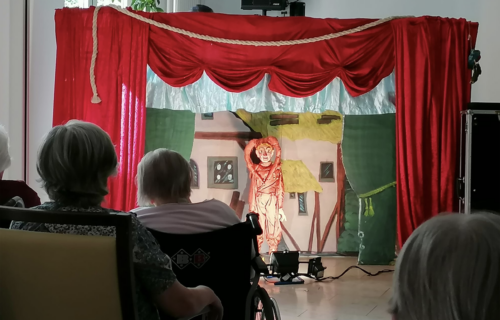 Puppentheateraufführung mit rotem Vorhang und Zuschauern, die gespannt die Bühne beobachten.