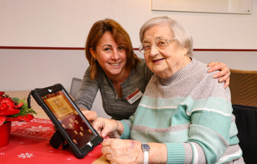 Eine Seniorin und Betreuungskraft nutzen ein Tablet in einem gemütlichen Raum.