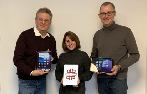 Drei Personen halten Tablets in der Hand, lächelnd vor neutralem Hintergrund. Digitalisierung und Technologie im Fokus.